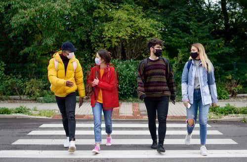 group of four friends walking in crosswalk wearing protective masks